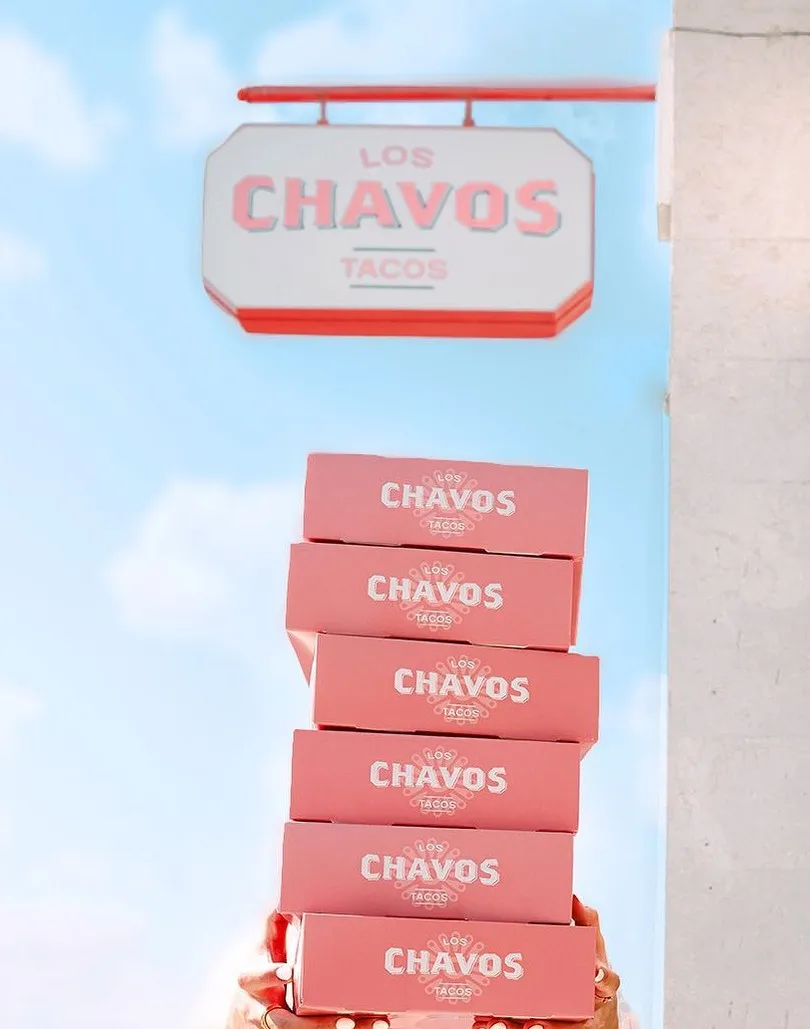 Letrero colgante con el logotipo y, debajo, una pila de seis cajas con el logotipo en brazos de una persona.
