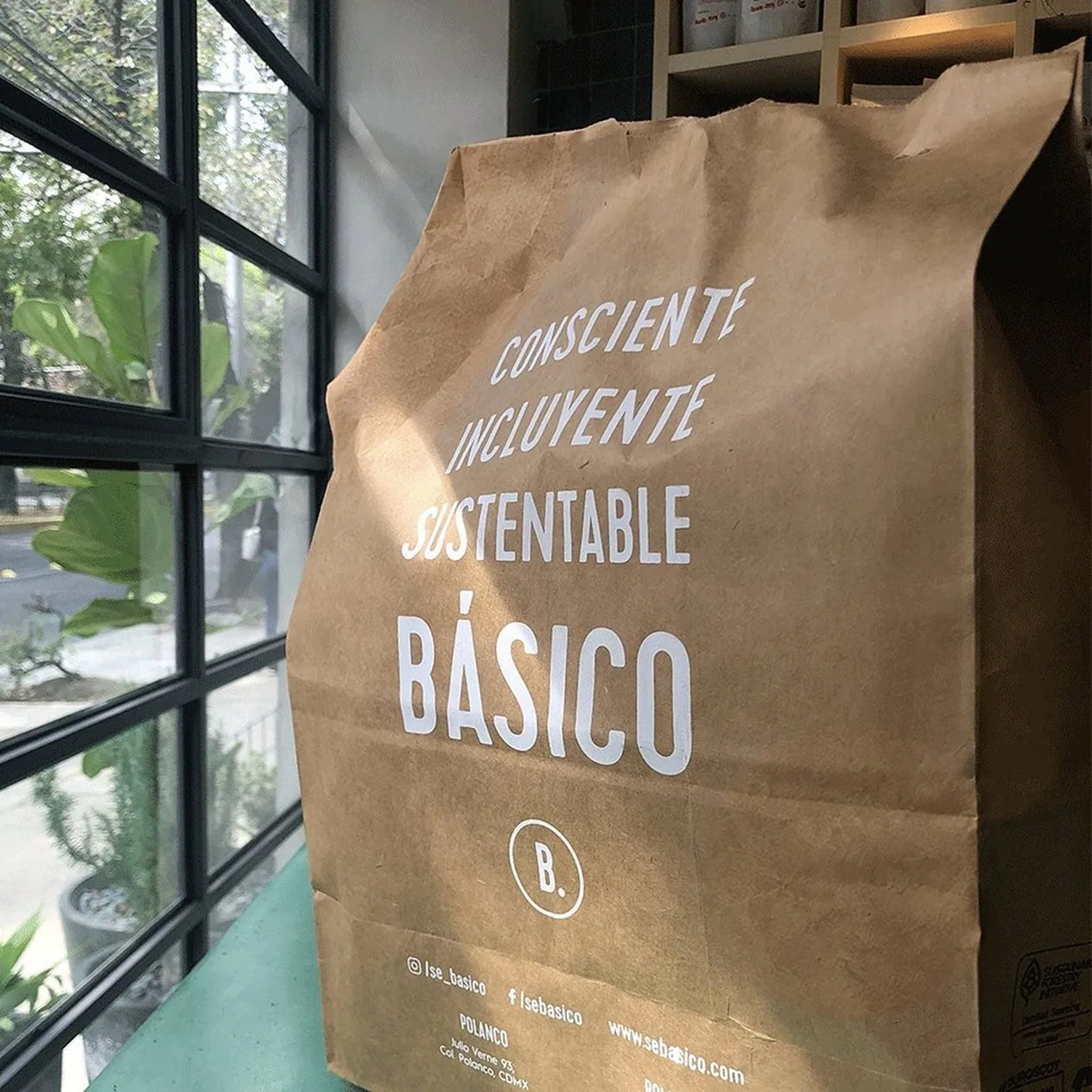 Bolsa de papel kraft con «Consciente, incluyente, sustentable», BÁSICO y la B. impresos en blanco.